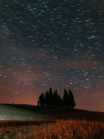 Starry sky over San Quirico d'Orcia cypresses at night. Famous location in Tuscany, Italy.