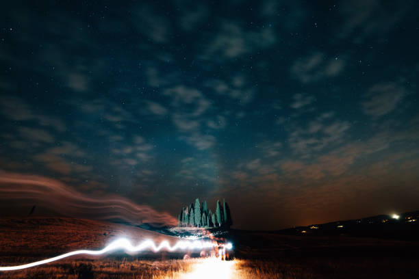 Starry sky over San Quirico d'Orcia cypresses at night. Famous location in Tuscany, Italy. Light trails.