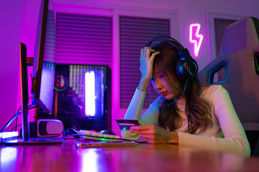 Top up online game with credit card concept. Gamer and E-Sport online of Asian woman playing online computer video game with lighting effect, broadcast streaming live at home. Gamer and E-Sport gaming