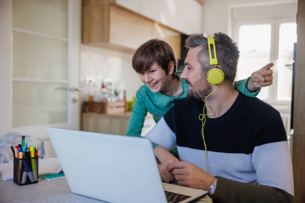 man working on laptop at home, his son distracting him from behind and laughing - inconvenience meeting business distracted imagens e fotografias de stock