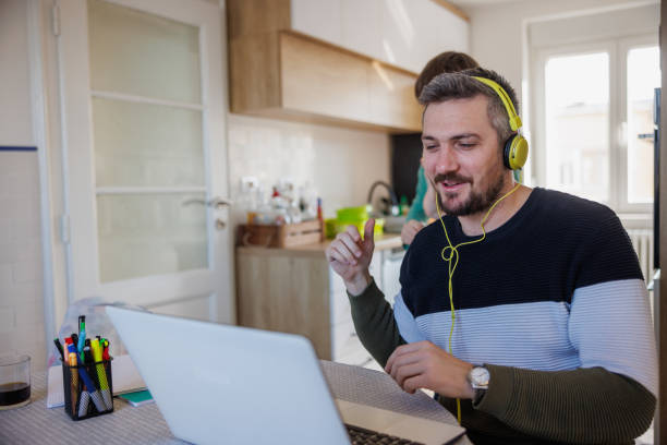 mężczyzna uśmiechnięty i pracujący na laptopie w domu, jego syn rozprasza go stojąc z tyłu - inconvenience meeting business distracted zdjęcia i obrazy z banku zdjęć