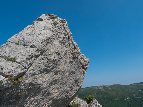 Big limestone boulder at heel of Perda Liana, rock formation on green forest hill, sardinian table mountain. National Park of Barbagia, Central Sardinia, Italy, summer day.