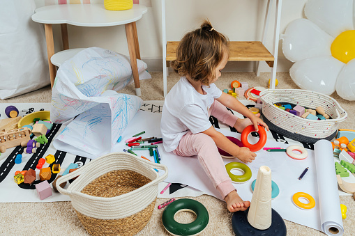Una niña sentada en el suelo juega con una pirámide de juguete y anillos de colores en la sala de juegos. Juego educativo para bebés y niños pequeños en la guardería moderna. Desorden en la habitación de los niños photo