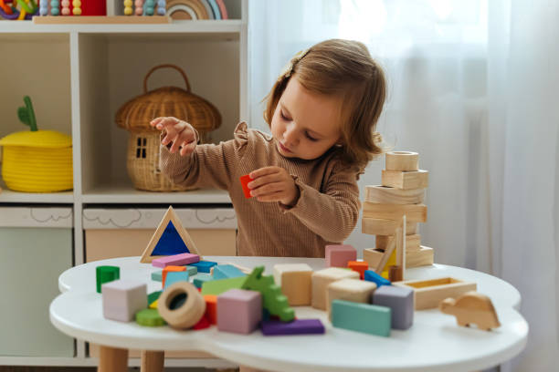 A little girl playing with wooden blocks on the table in playroom.  Educational game for baby and toddler in modern nursery. The kid builds a tower from wooden rainbow stacking blocks. A little girl playing with wooden blocks on the table in playroom.  Educational game for baby and toddler in modern nursery. The kid builds a tower from wooden rainbow stacking blocks. montessori stock pictures, royalty-free photos & images