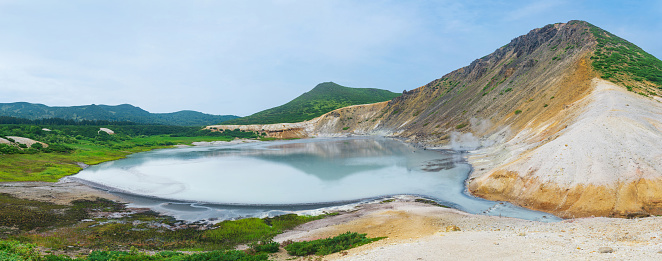 panorama of a hot mineralized lake with thermal spring and smoking fumaroles in the caldera of the Golovnin volcano on the island of Kunashir