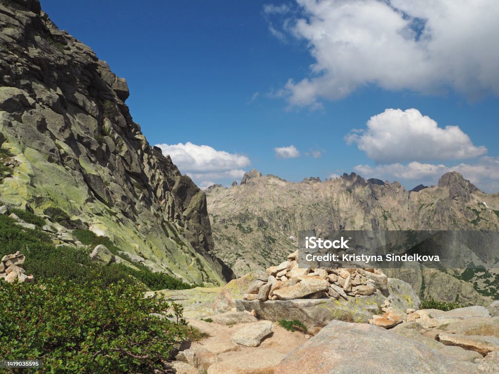 scenery of high mountainn peaks in corsician alpes with green bushes and rocks pile cairn marked path to summit monte rotondo and white clouds blue sky Beauty Stock Photo