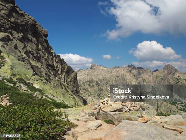 Scenery Of High Mountainn Peaks In Corsician Alpes With Green Bushes And Rocks Pile Cairn Marked Path To Summit Monte Rotondo And White Clouds Blue Sky Stock Photo - Download Image Now