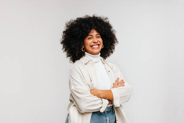 Gorgeous woman with an Afro hairstyle smiling at the camera Gorgeous woman with an Afro hairstyle smiling at the camera while standing against a white background. Happy young woman of colour wearing her curly hair with confidence. woman arms folded stock pictures, royalty-free photos & images