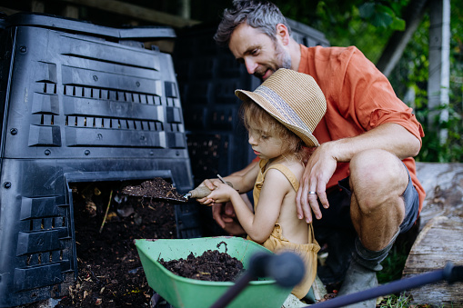 Father with his daughter putting compost out of a composter, farmer lifestyle.