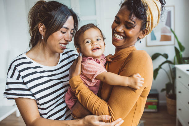 Gay couple with baby at home Young mothers playing with baby girl in living room. lesbian couple embracing stock pictures, royalty-free photos & images