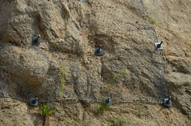reinforcing slope with steel net anchored deep into rock. falling loose rock stones do not fall on road. anchored with steel nails with nuts. drilled into subsoil and fasten the mesh, train track, anchor, anchoring, reinforced, screwed, stabilization, reinforcing, slip, land, notch, rod