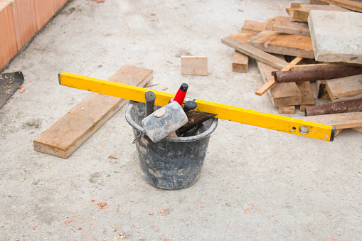 Bucket of masonry tools next to a brick wall at a new family home construction site. This image is part of a series.