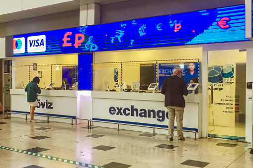 Two people exchanges money and currency exchange kiosk at Anyalya Airport arrival hall in Turkey