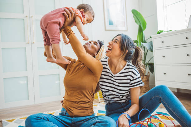 Gay couple with baby at home Young mothers playing with baby girl in living room. lesbian stock pictures, royalty-free photos & images