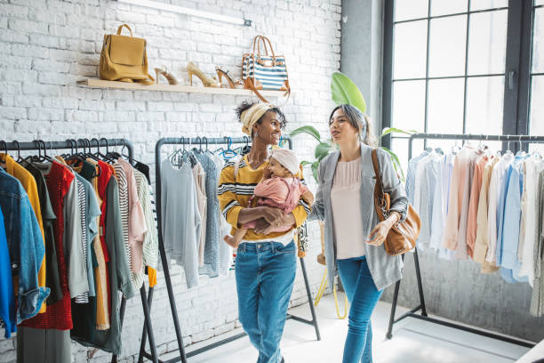 Gay couple in shopping with baby Young female gay couple at thrift store with baby girl, talking and choosing clothes. baby boutique stock pictures, royalty-free photos & images