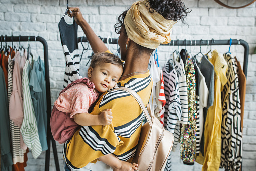 Young woman with baby girl at thrift store, choosing clothes.