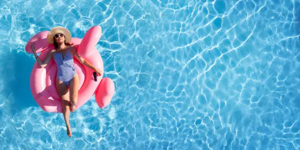 Woman relaxing on pink flamingo inflatable ring. Sunny pool vacation. Flat lay with copy space
