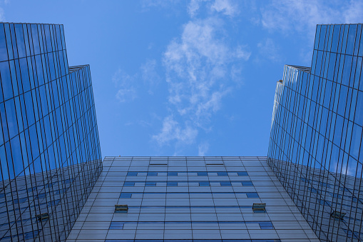 Bottom view of a modern glazed tower with blue sky in the background. Natural lighting with shadows on buildings.