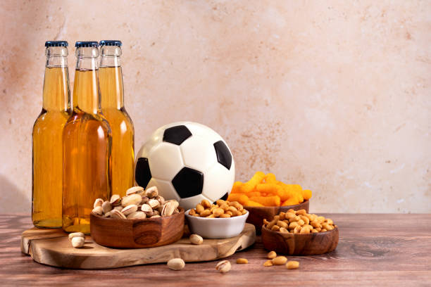 cerveja e lanche em mesa de madeira com bola de futebol, comida noturna de jogo de futebol - american football football food snack - fotografias e filmes do acervo