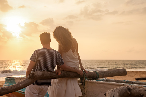 Young multi-racial couple walking together embracing on the beach during sunset