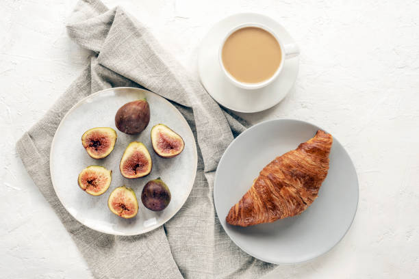 Healthy breakfast with coffee cup, croissant and figs on white textured table. Top view, flat lay