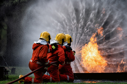 In Industry safety fire fighter team department on  training fight with gas and oil fire by hold hose together spray jet turbulence water and foam to extinguish remove oxygen