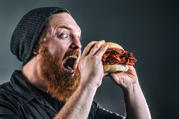 Burly Bearded Man Devouring a Bacon Sandwich stock photo