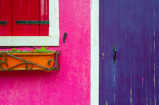 Pink painted facade with window and violet wooden door. Colorful architecture in Burano island, Venice, Italy.