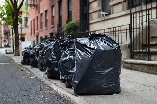 A row of black garbage bags along a residential street and sidewalk waiting to be picked up in Greenwich Village of New York City