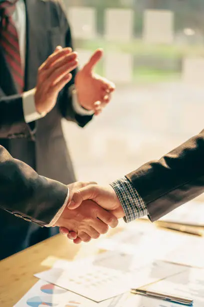 Young businessmen shake hands after a short job to sign a co-working business contract in a modern office with vintage-style images of colleagues at a teamwork meeting.
