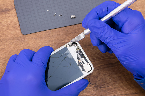close-up of a smartphone screen repair, on a wooden background, fragments are removed from the case with a scalpel