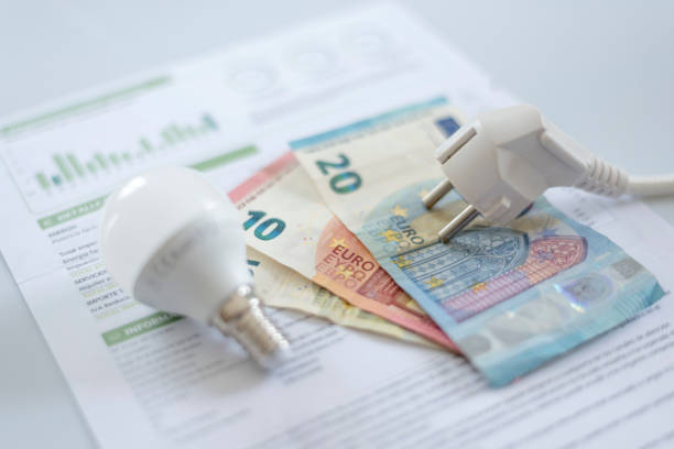 una gorra eléctrica blanca, una bombilla y billetes en euros en una factura de electricidad. aumento en el costo de la electricidad para clientes residenciales y usuarios comerciales. pago de facturas de luz. aumentar el concepto de precios de la electric - altas luces fotografías e imágenes de stock