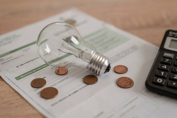 istock Electricity bill with light bulb, several coins and calculator on the desk. Concept of electricity prices and tax payments 1419070833