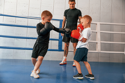 Fighting on the ring. Young tattooed coach teaching the kids boxing techniques.