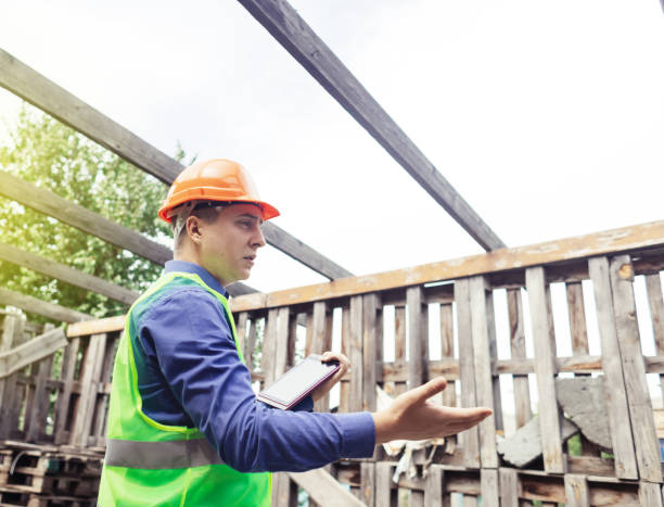 istock Building inspector. Man in a hard hat and a yellow reflective vest examines damaged structures and inspects the building. Damage assessment. Preparing for the repair or construction of a building 1419072868
