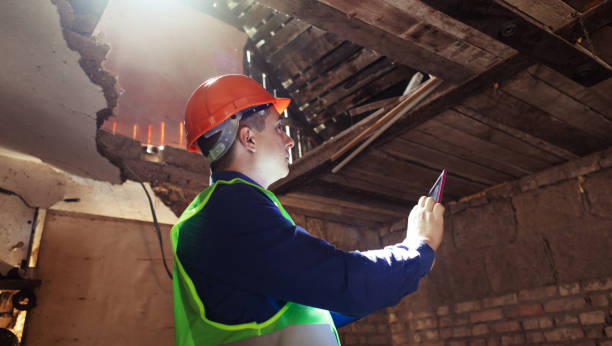 istock Building inspector. Man in a hard hat and a yellow reflective vest examines damaged structures and inspects the building. Damage assessment. Preparing for the repair or construction of a building 1419074041