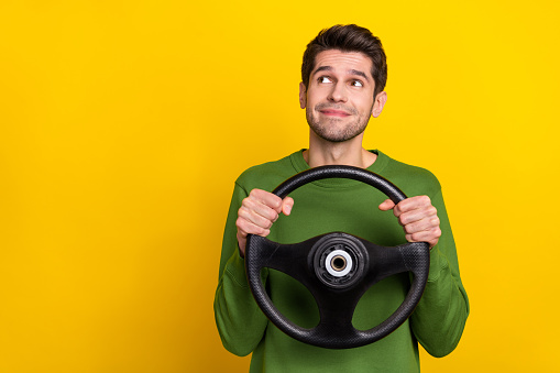 Photo of funny dreamy young guy dressed green pullover holding steering wheel looking empty space isolated yellow color background.