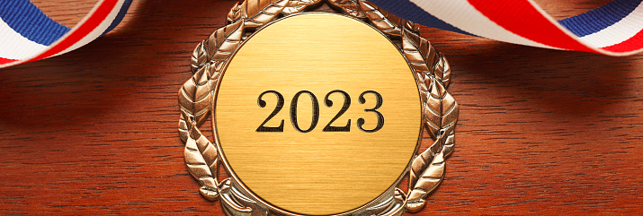 Gold medal engraved with the year 2023 rests on a wood desk.