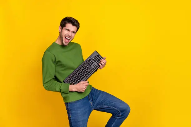 Photo of funny funky guy dressed green pullover playing keyboard empty space isolated yellow color background.
