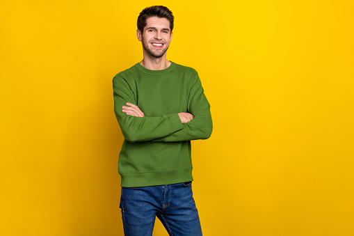 Photo of attractive charming young guy wear green sweater arms crossed empty space isolated yellow color background.