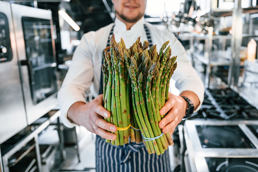 Man holding asparagus. Chef is on the kitchen preparing food.