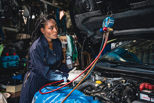 Professional female mechanic analyzing the problem by using a manifold gauge to measure the air conditioner pressure in the garage.