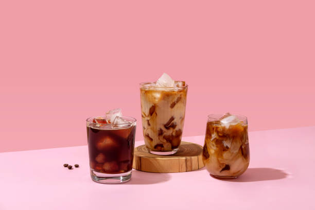 кофе со льдом в высоком стакане с налитыми сливками и кофейными зернами. набор с различными видами кофейных напитков на розовом столе. - latté стоковые фото и изображения
