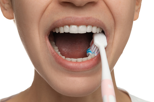 Woman brushing teeth with paste on white background, closeup. Dental care