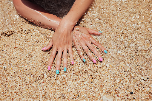 Unrecognizable woman hands with pink and blue manicure nails on sandy beach background