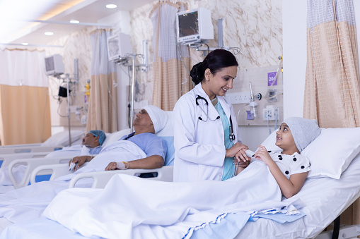 Smiling doctor embracing recovering girl lying on bed. Friendly healthcare provider consoling female patient. They are at ward in hospital during diagnosis.