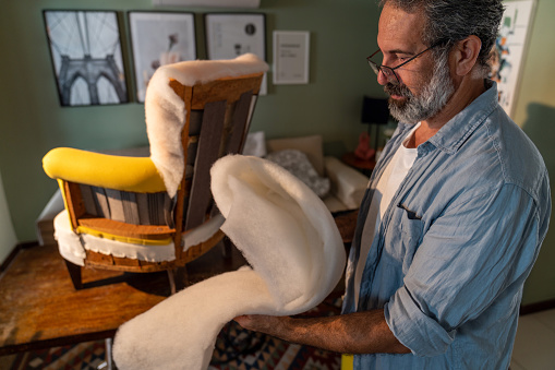 A nimble elderly man is reupholstering an armchair at home