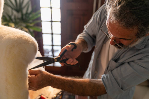Mature craftsman engaged in repair of vintage furniture, reupholstering chair in living room
