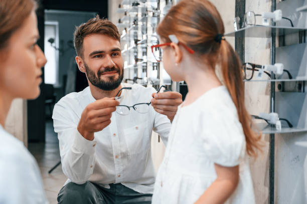 Family is together. Woman, man and little girl is choosing right glasses for correcting vision stock photo