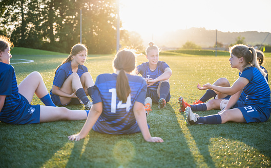 Female soccer players relaxing on grass field after practice. Sport and healthy lifestyle concept.
